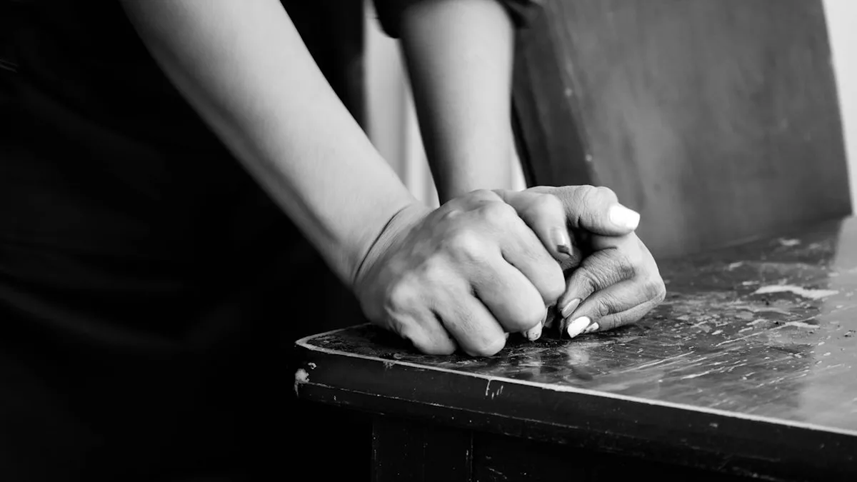 Un homme et une femme face à face dans la pénombre dorée d'un salon, leurs mains presque jointes sur une table, deux verres de vin à moitié vides