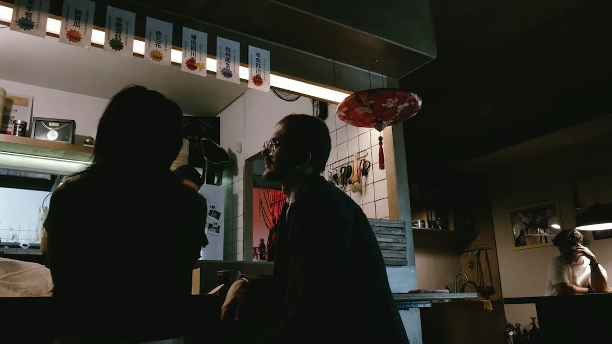 Une femme et un homme face à face à une table de café, un sourire discret, deux verres posés entre eux