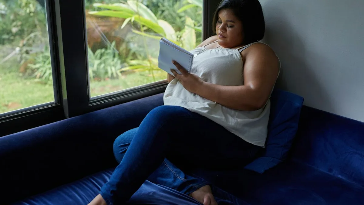Une femme assise sur un canapé près d'une fenêtre relit les réponses notées dans un carnet