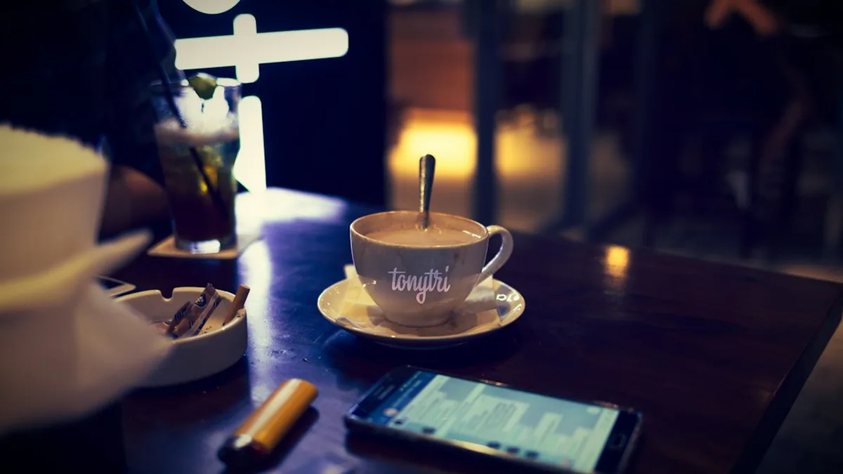 Un téléphone posé sur une table de café, à côté de deux verres, dans une lumière chaude de fin de journée